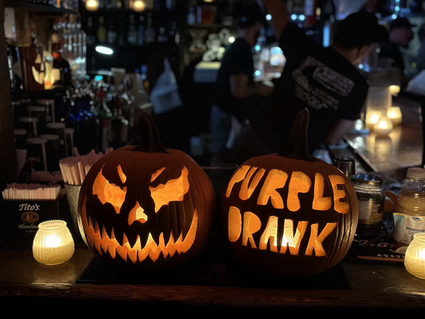 Carved jack-o'-lanterns spelling Purple Drank on the bar at night